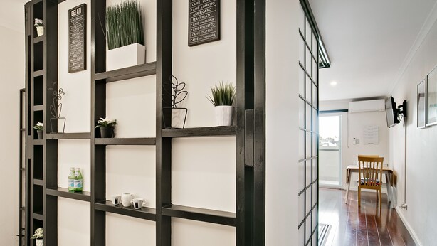 A modern interior with a black-framed shelving unit displaying potted plants and a menu board. - Newtown Mews (Newtown)