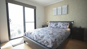 A bedroom with a bed, a nightstand, a lamp, and a sliding glass door leading to a balcony. - Newtown Mews (Newtown)