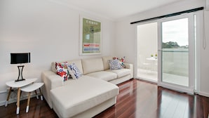 A modern living room with a sofa, a small table with a lamp, and a poster on the wall. - Newtown Mews (Newtown)