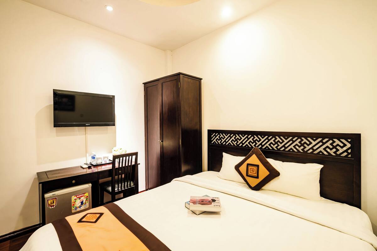 A hotel room with a bed, a desk, a television, and a wardrobe.