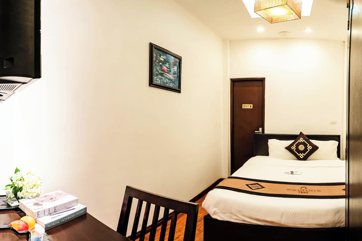 A hotel room with a bed, a desk with a chair, a framed picture on the wall, and an exit sign.
