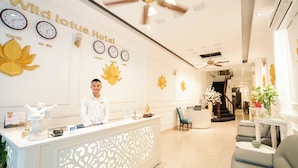 A reception area with a white reception desk, a man standing behind it, and clocks displaying times for Tokyo, Ha Noi, London, Sydney, and Paris. - Wild Lotus Hotel & Travel 2 (Hanoi)