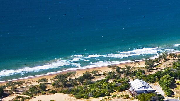 An aerial view of a coastal area with a beach, ocean waves, and sparse vegetation. - Loka Santi (Agnes Water)