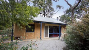 A small, single-story building with a metal roof and blue trim, surrounded by dense vegetation. - Split Point Cottages (Aireys Inlet)