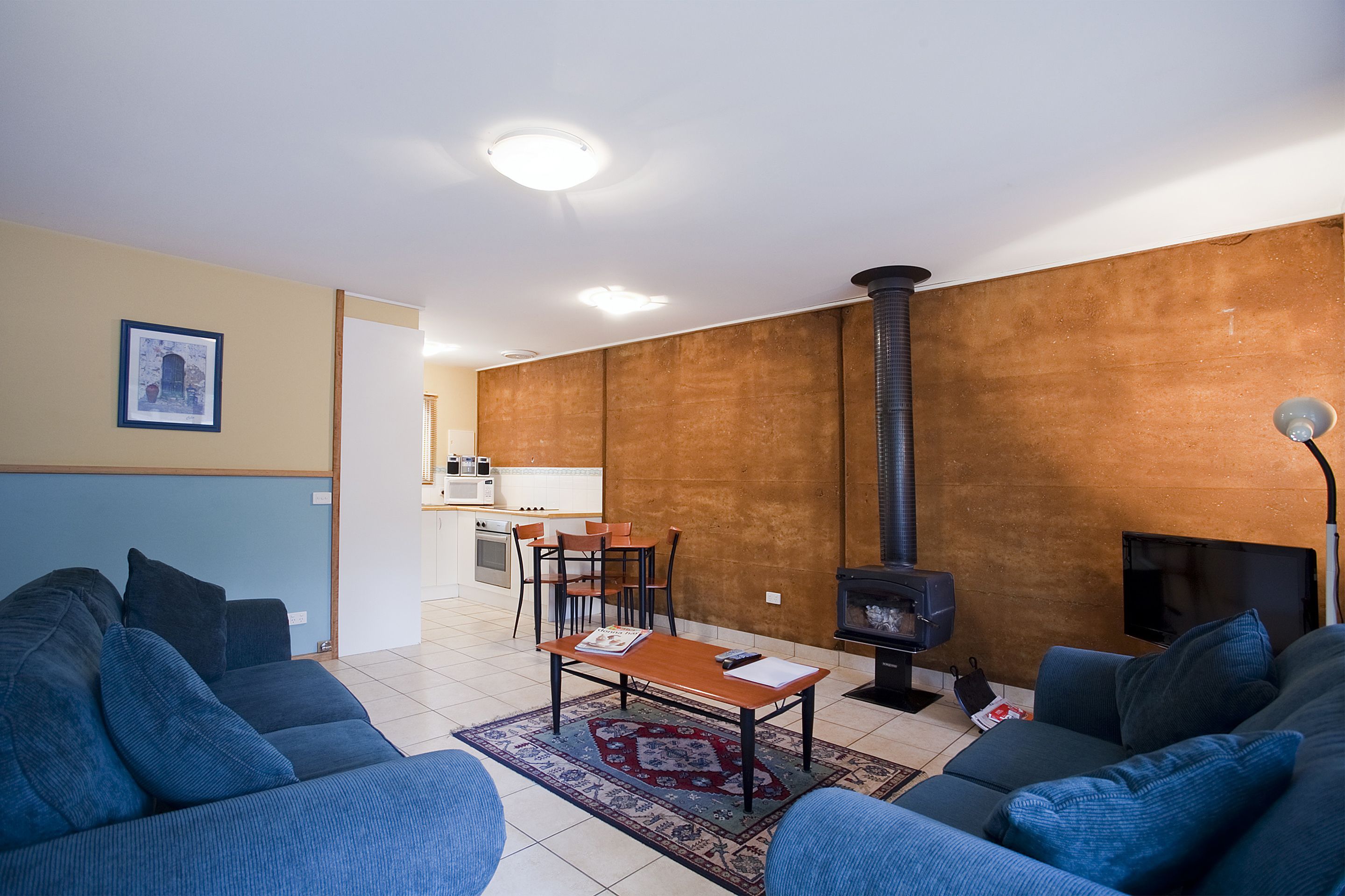 A living room with a sofa set, a coffee table, a fireplace, and a kitchen area in the background.