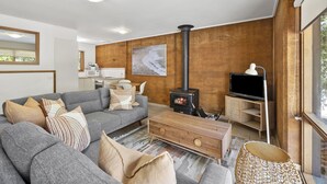 A modern living room with a grey sofa, wooden coffee table, and a TV stand. - Split Point Cottages (Aireys Inlet)