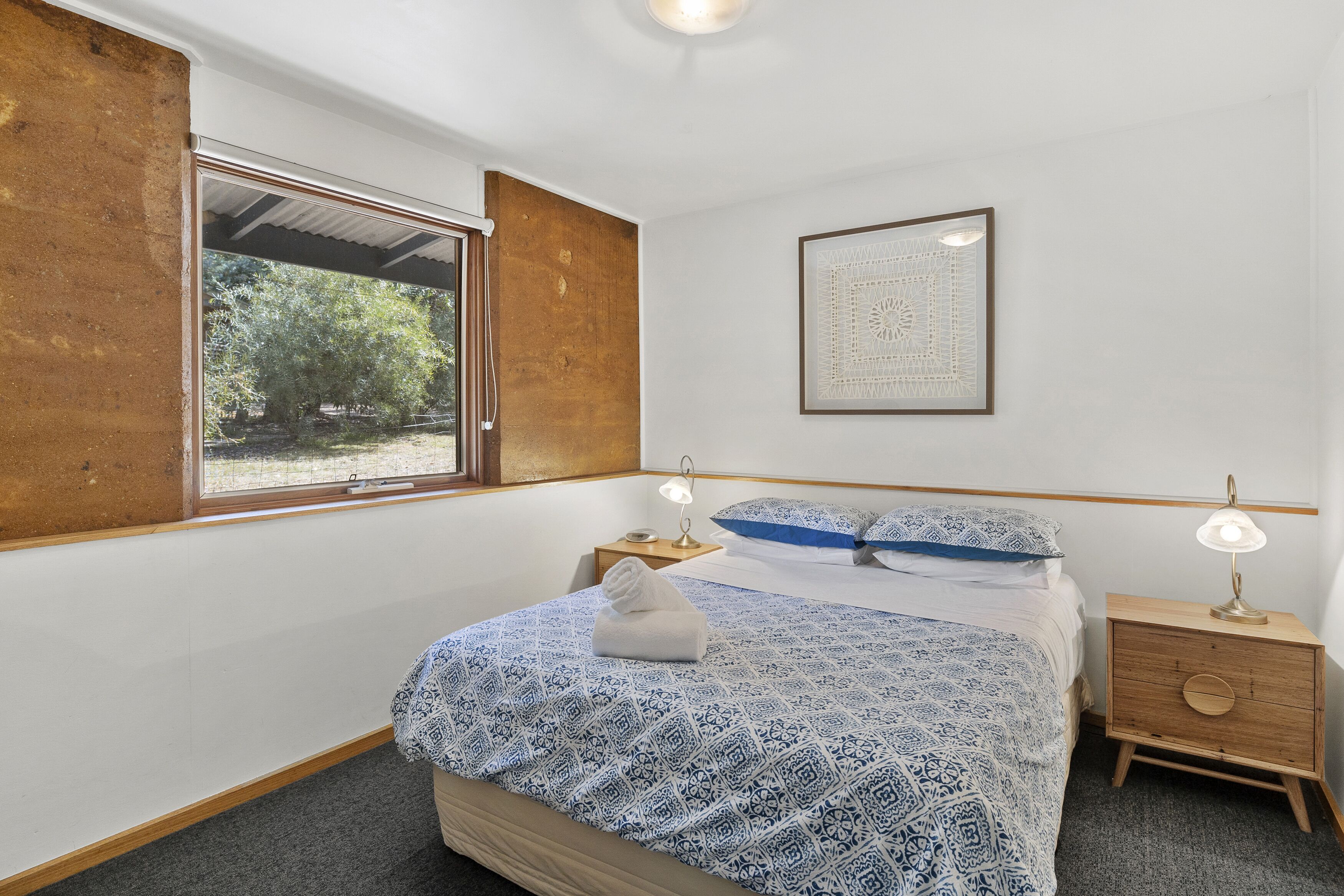Une chambre à coucher comprenant un lit, une table de chevet, une commode, une fenêtre et une œuvre d’art accrochée au mur.