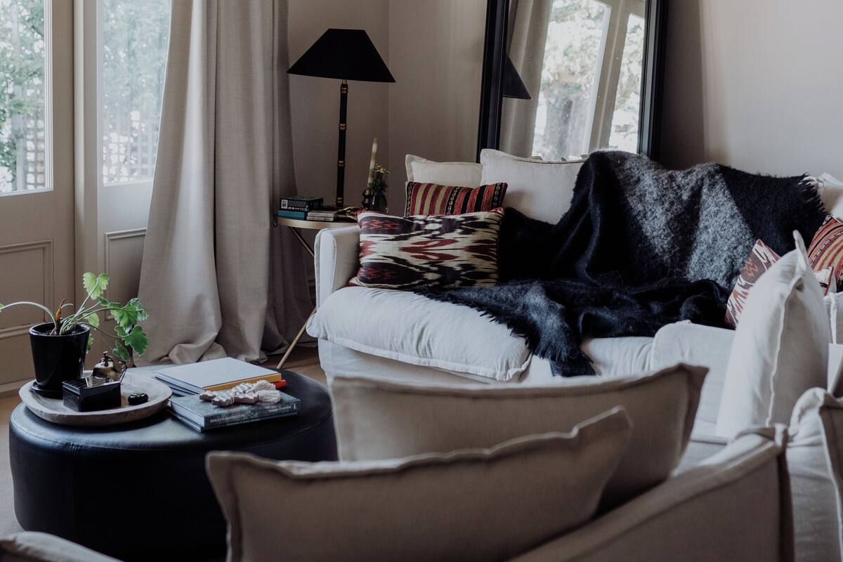 A living room with a large window, a sofa, a coffee table, a lamp, and a mirror.