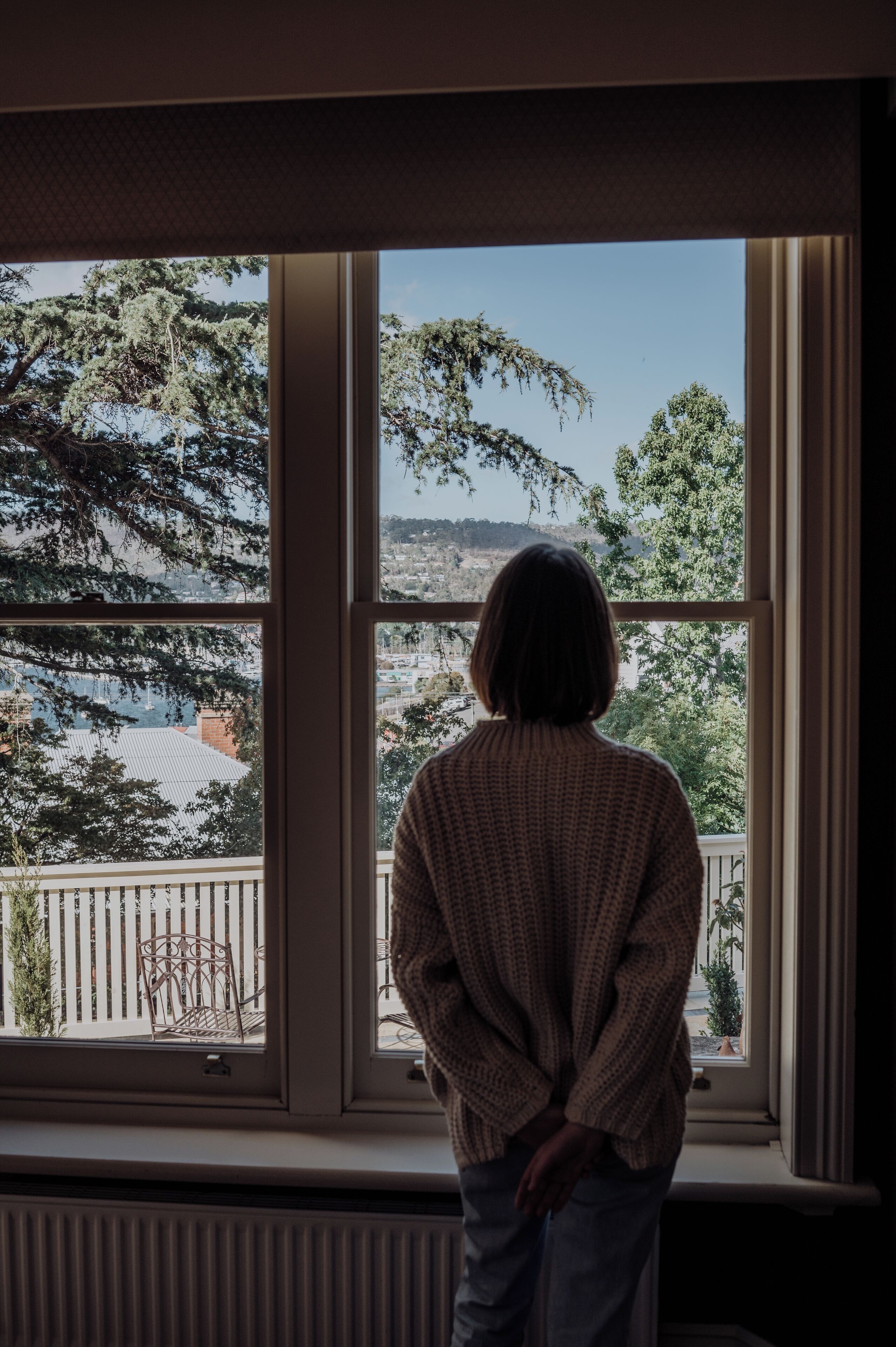 A person standing by a window with a view of trees and a distant landscape.