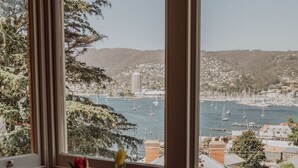 Una mesa de comedor con un pastel, un juego de té y un jarrón con flores, y una vista de una bahía con barcos.