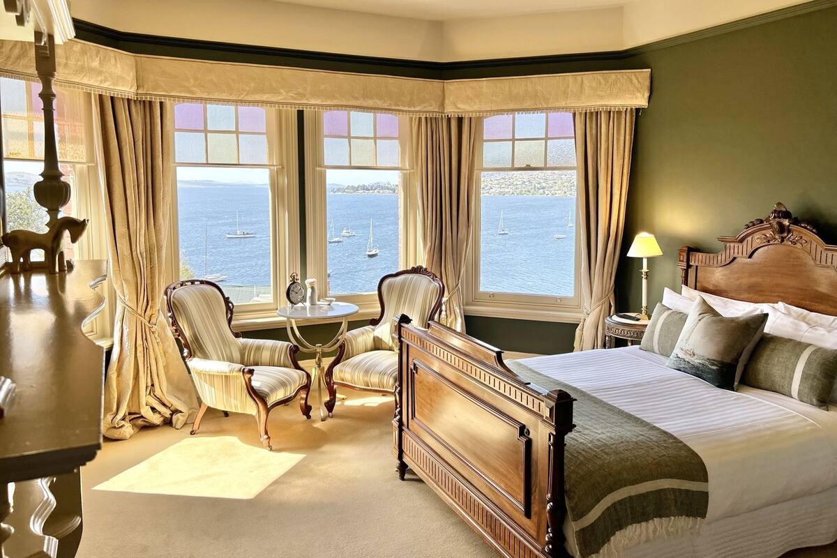 A hotel room with a large bed, two armchairs, a small table, and a view of the sea.