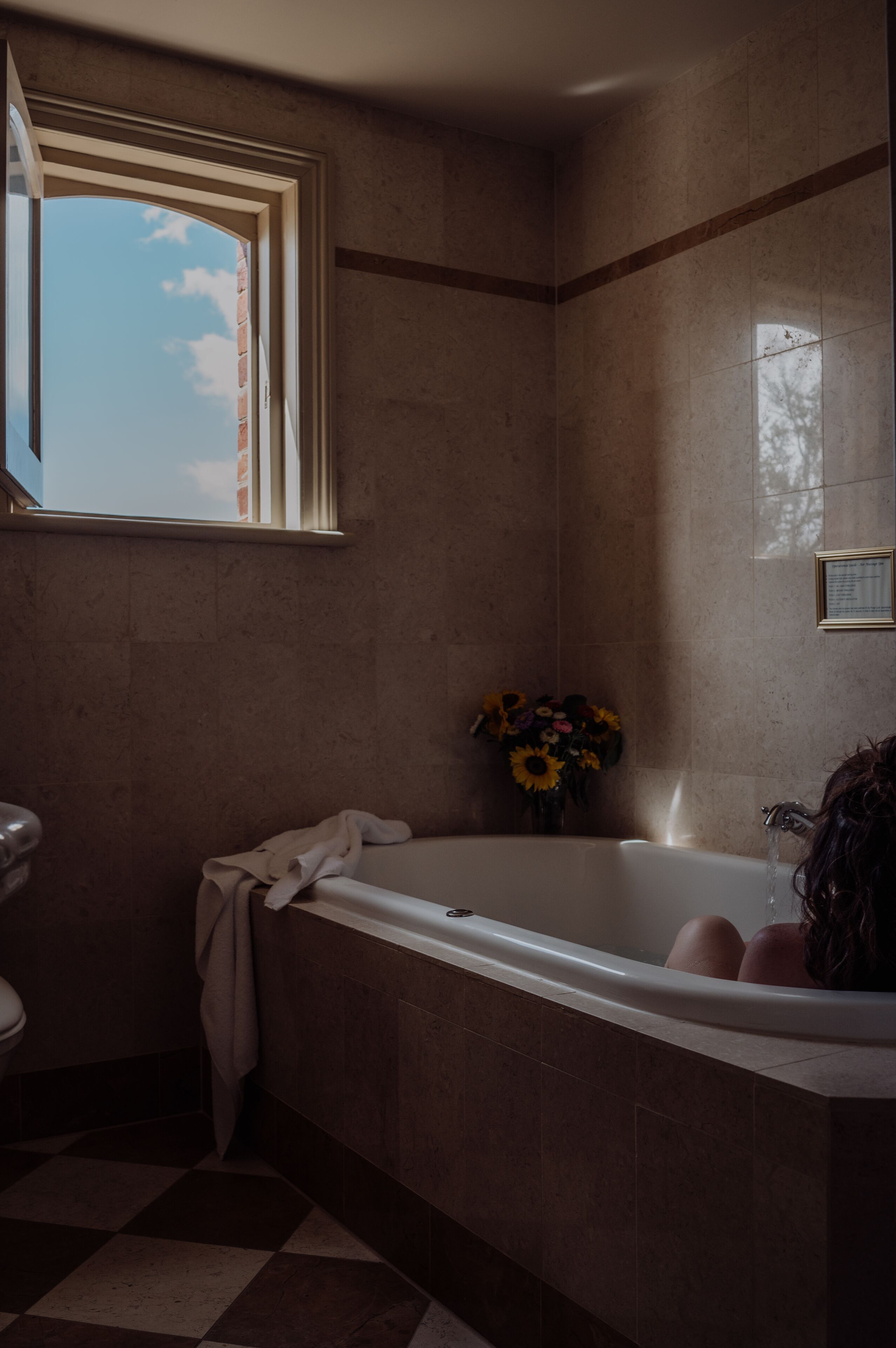 Une salle de bain avec une baignoire, une fenêtre et un vase de fleurs.