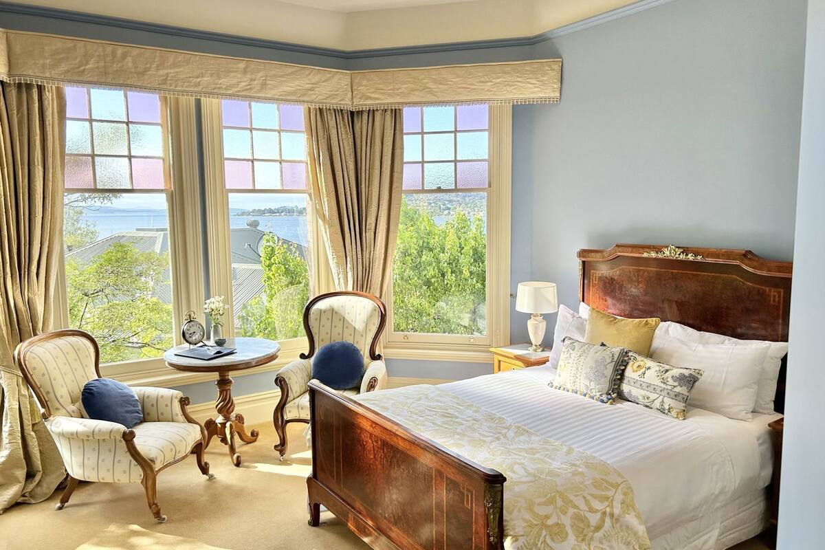 A bedroom with a large bed, two chairs, a table, and a view of the outdoors.