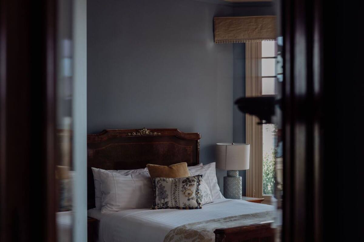 A bedroom with a wooden bed, white bedding, a bedside lamp, and a window with a view.