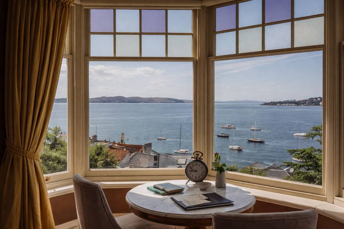 A room with a bay view, a round table with a clock, and a chair.