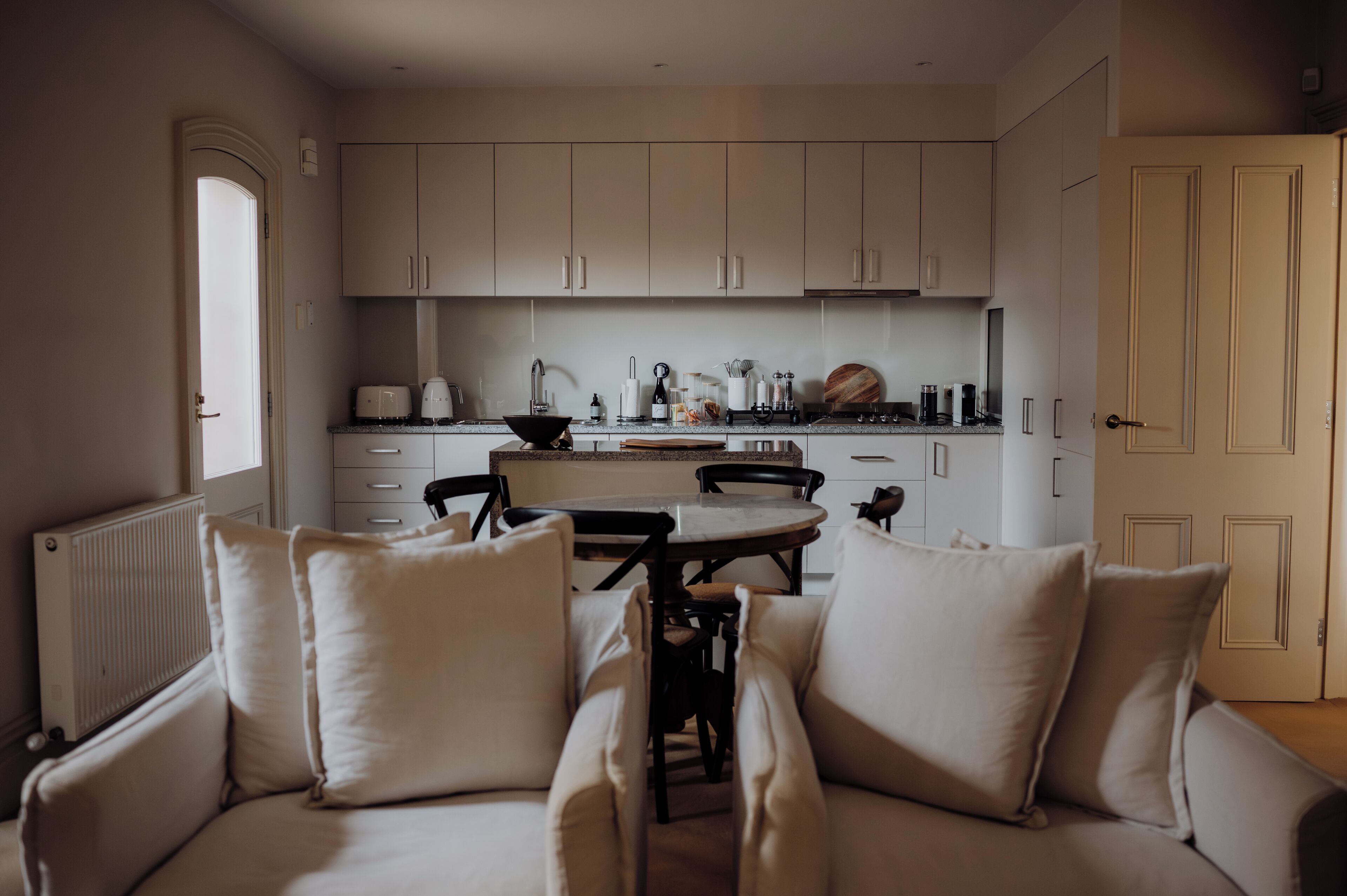 A modern kitchen with white cabinets, a dining table with chairs, and a built-in oven.
