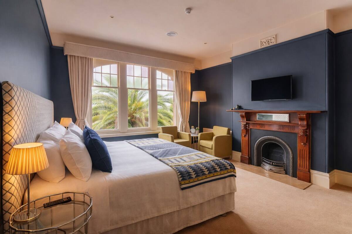 A hotel room with a bed, a television, a fireplace, and a window with curtains.