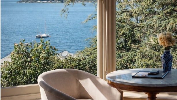 Una habitación con vistas a una masa de agua, una silla, una mesa con un jarrón y una ventana con vidrio esmerilado.