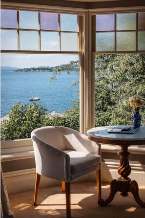 A room with a view of a body of water, a chair, a table with a vase, and a window with frosted glass. - Grande Vue Private Hotel (Battery Point)