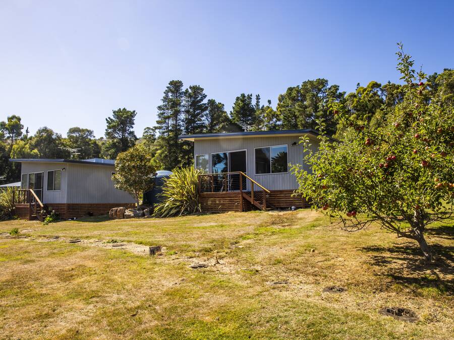 Two mobile homes with wooden decks and large windows, surrounded by trees and a grassy area.