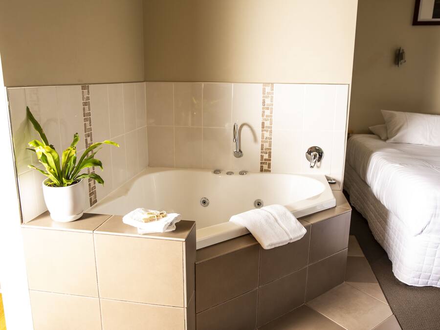 A modern bathroom with a large bathtub, a potted plant, and a neatly made bed.