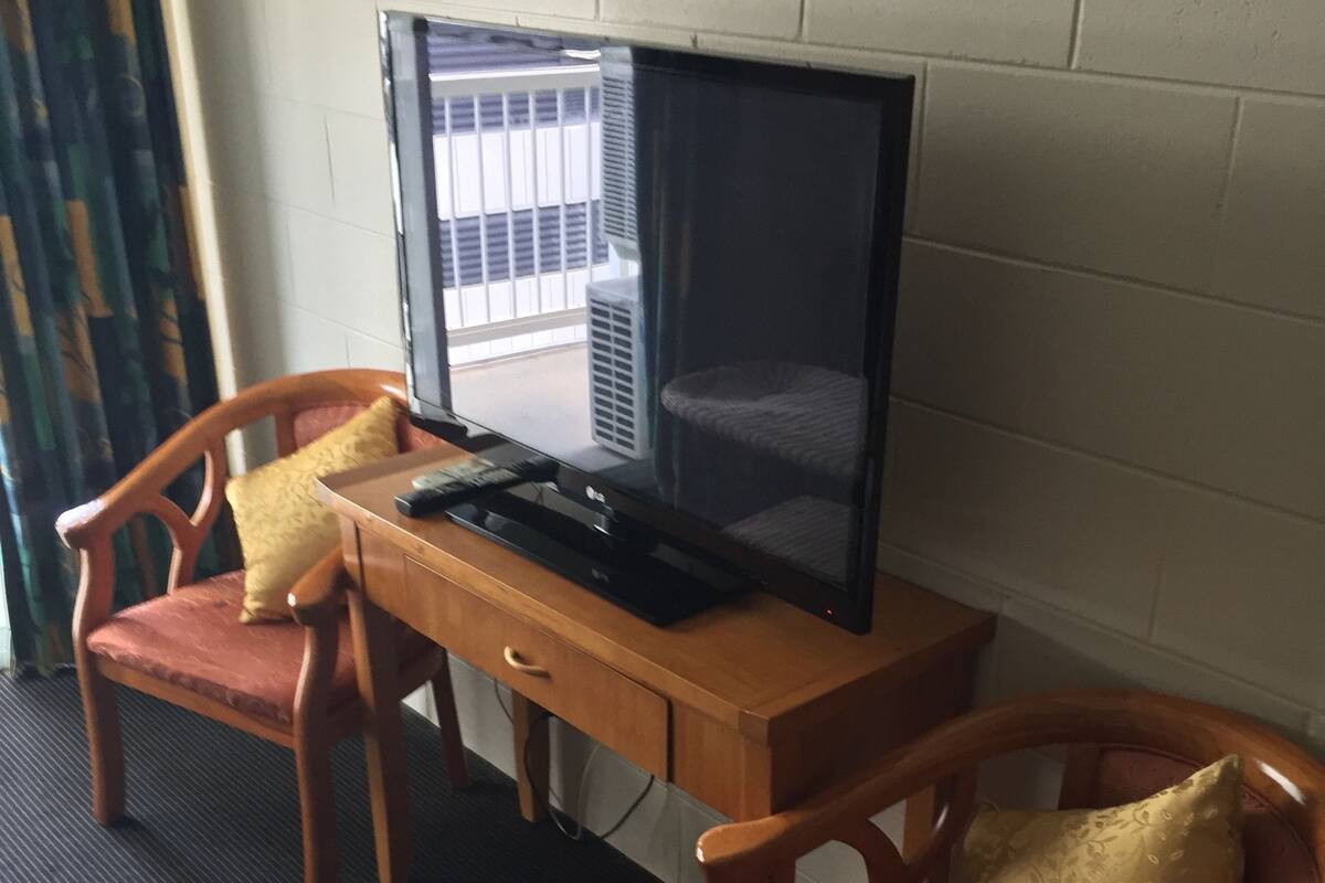 Een kamer met een houten bureau, een televisie en twee houten stoelen met kussens.
