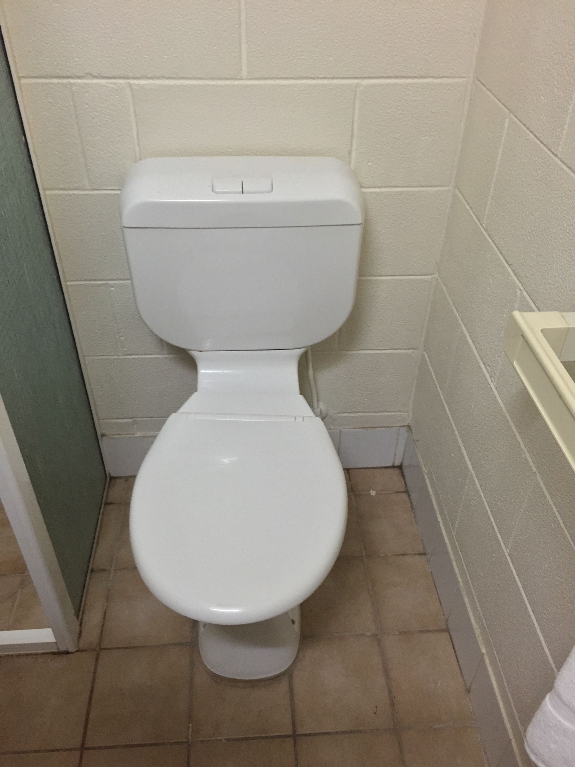 A white toilet in a bathroom with beige tiled walls and floor.