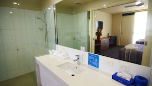 Une salle de bain d’hôtel avec une douche à parois de verre, un lavabo équipé de produits de toilette et un miroir qui reflète la pièce.