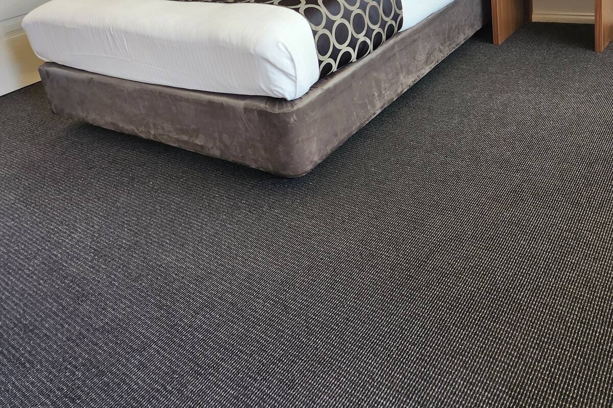 A hotel room with a large bed, a bedside table, and a carpeted floor.