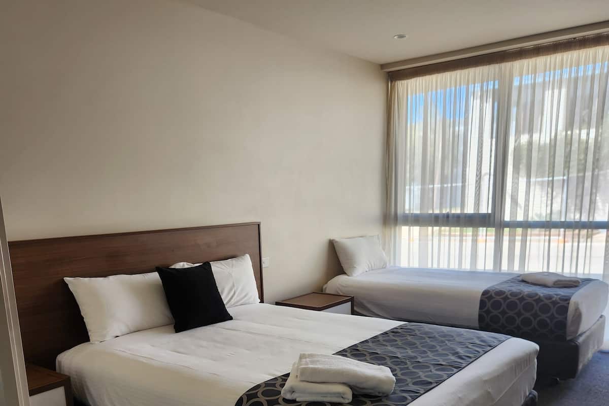 A hotel room with two beds, a ceiling fan, and a large window with curtains.