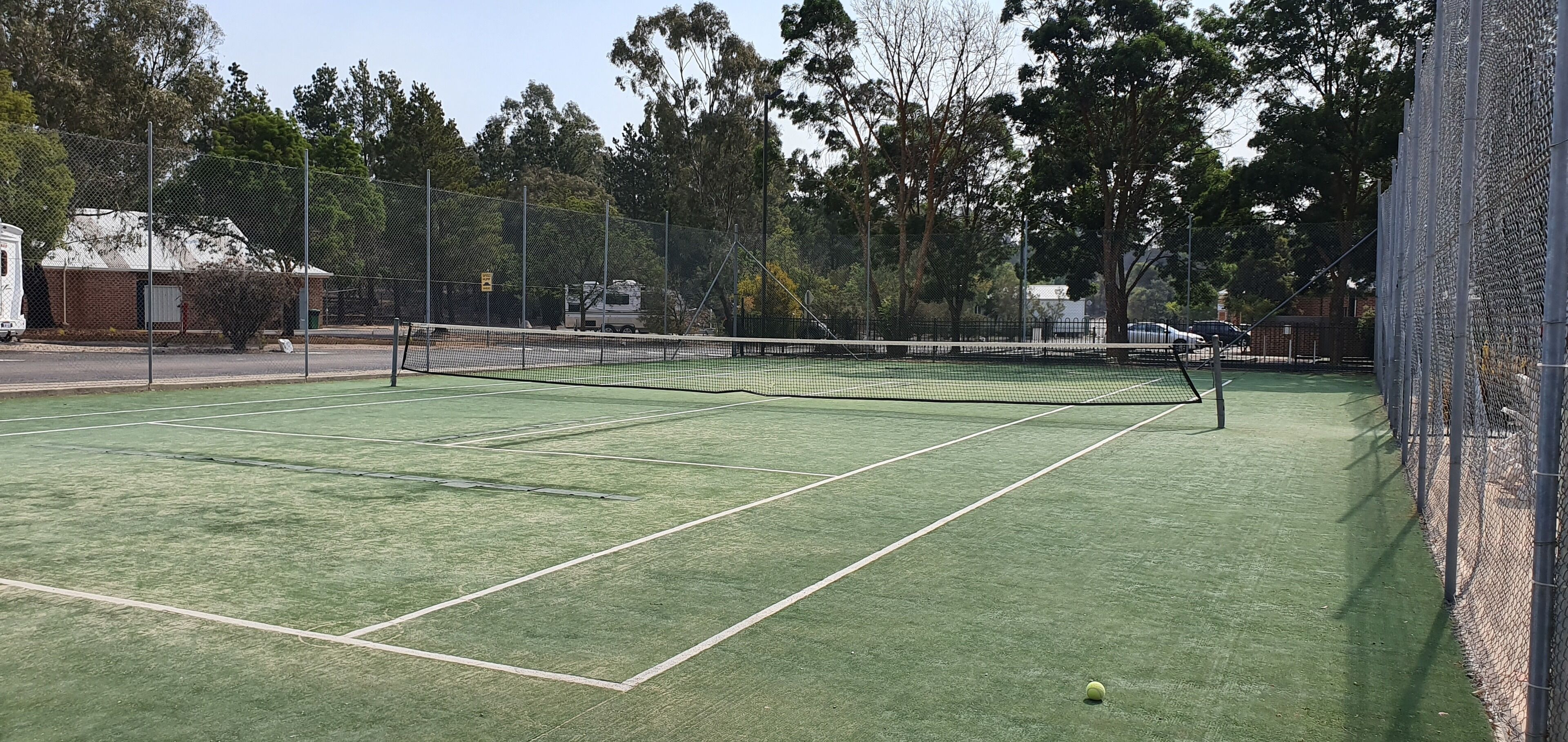 A tennis court with a net, surrounded by a chain-link fence and trees.
