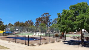 A fenced outdoor area with a pool, tennis court, and picnic tables.