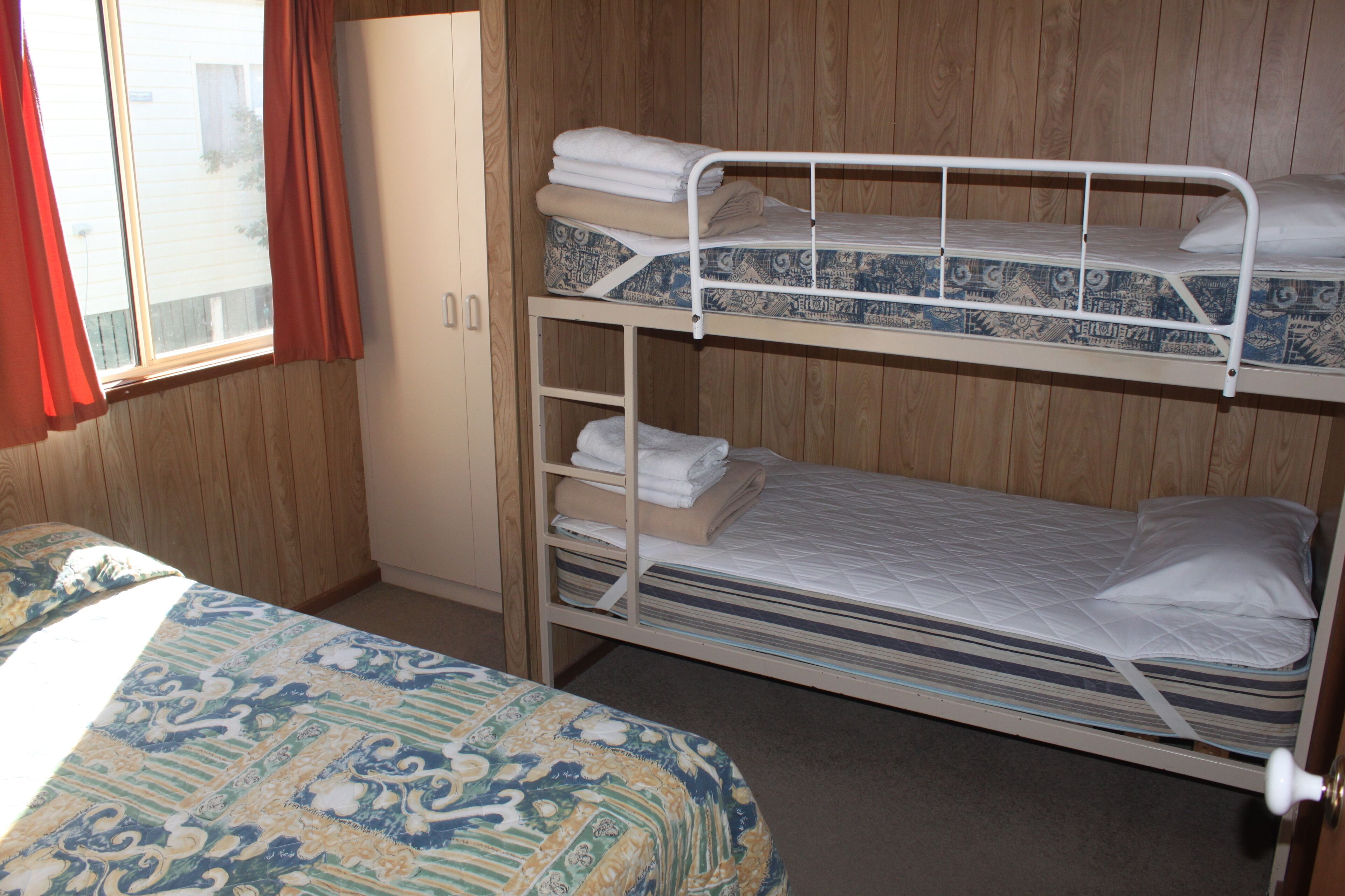 Een slaapkamer met een stapelbed, een geboeide spreideken, een kledingkast en een raam met gordijnen.