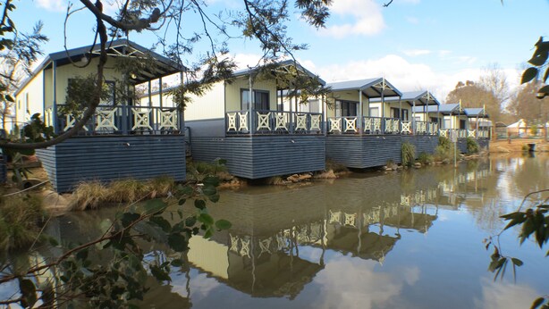 A row of mobile homes by a calm lake, with a clear sky above.