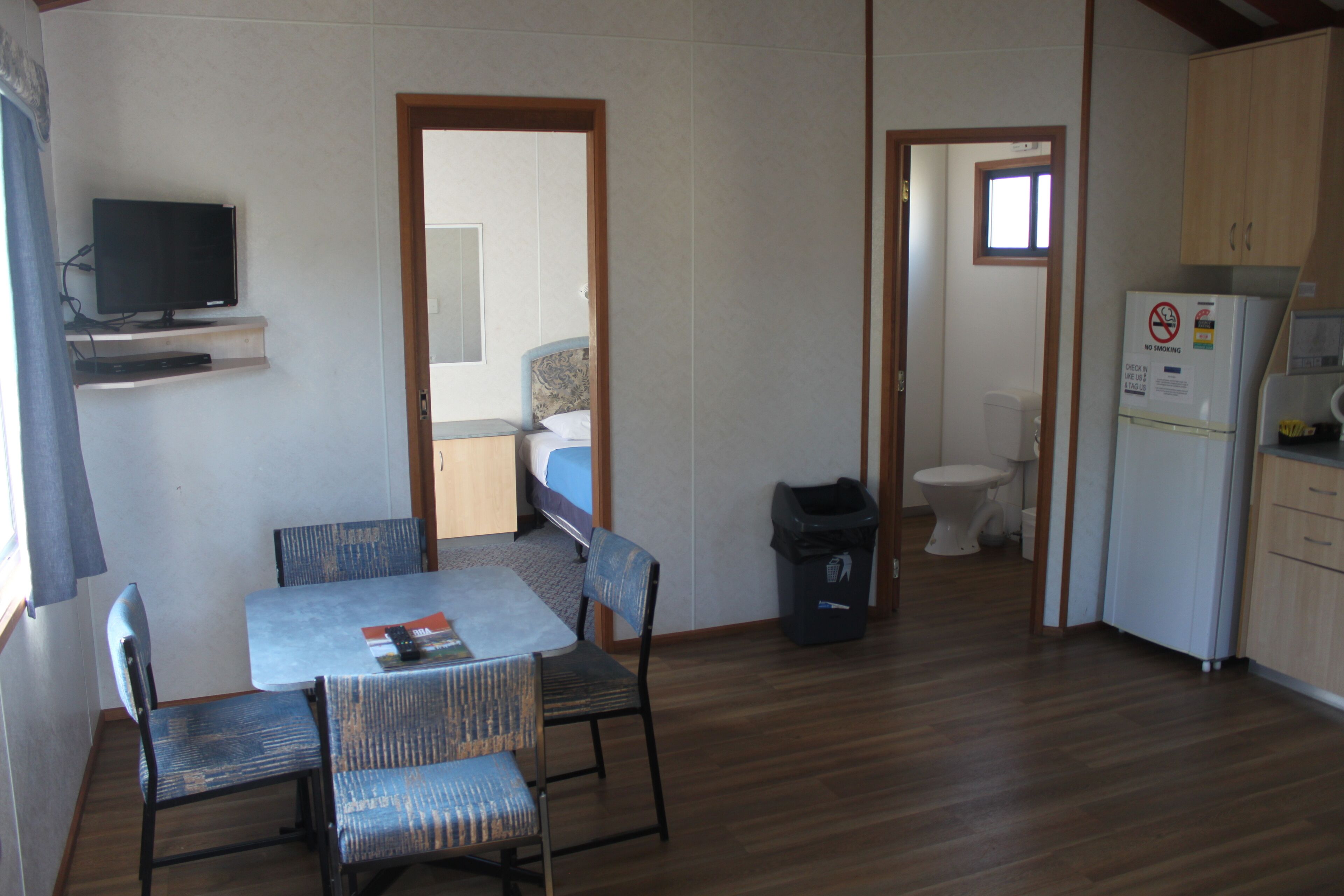 A compact room with a dining table, chairs, a television on a shelf, a small kitchenette, and a separate bathroom.