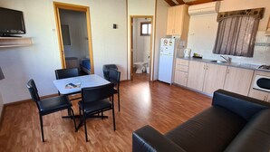 A compact living space with a dining table, chairs, a sofa, a kitchenette, and a television.