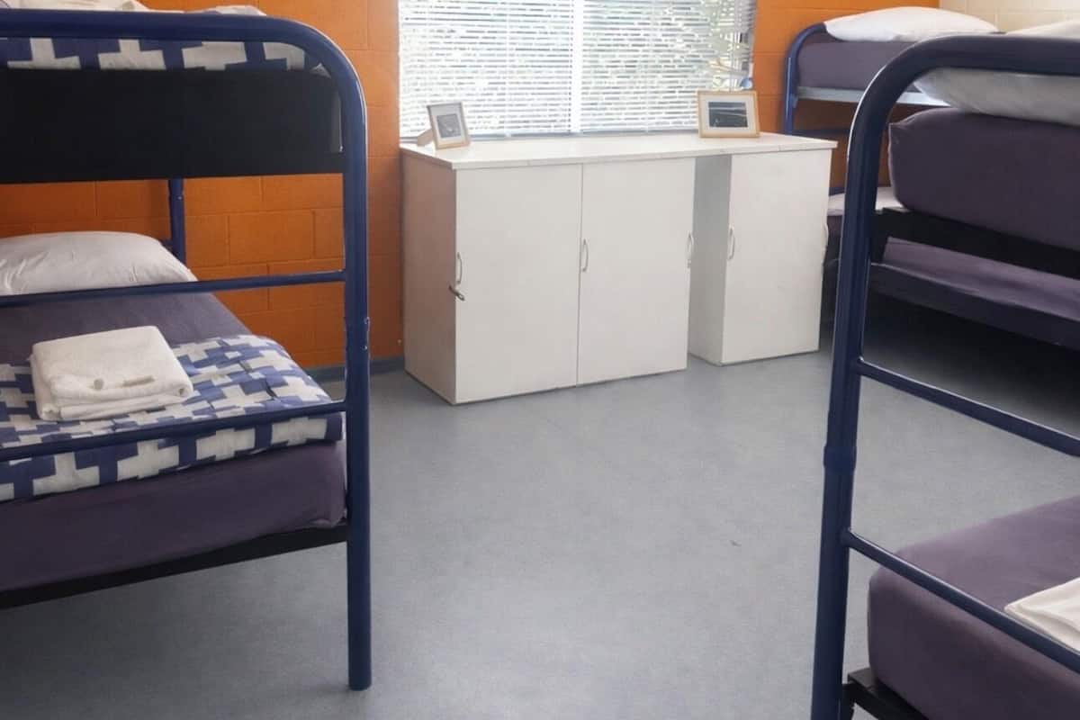 Habitación tipo dormitorio con literas, un escritorio y una ventana con persianas.