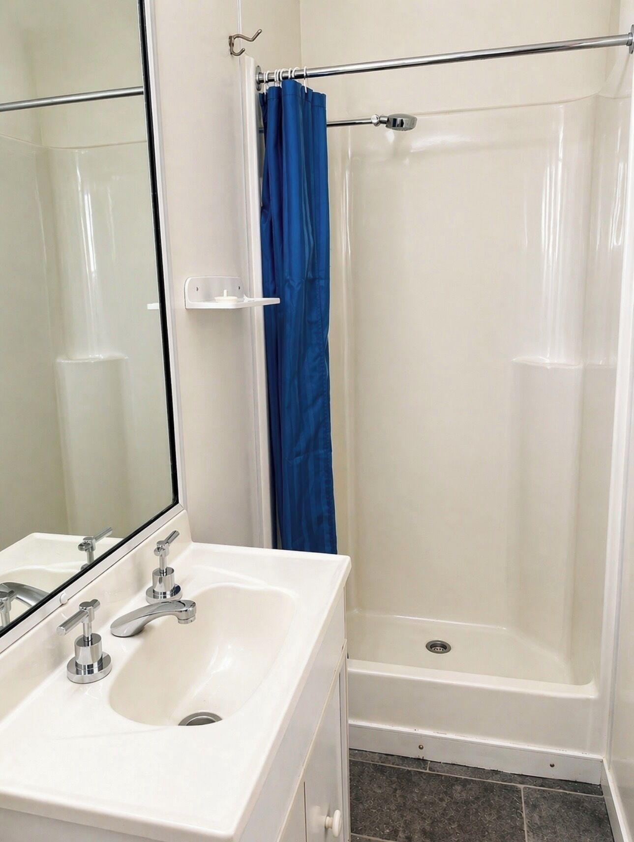 A bathroom with a white sink, a mirror, a shower with a glass door, and a blue shower curtain.