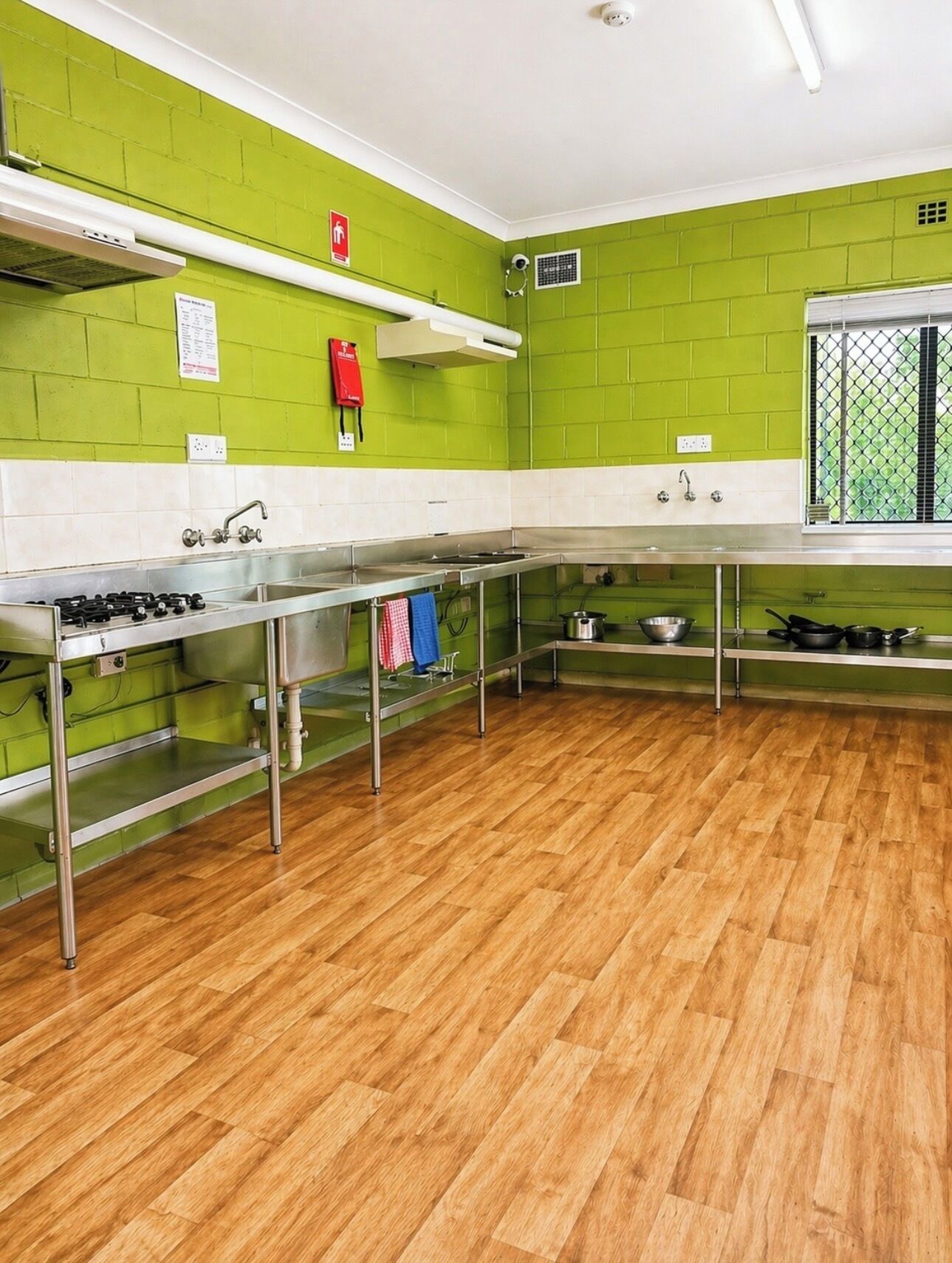 Een keuken met groene wanden, roestvrijstalen apparatuur en een houten vloer.