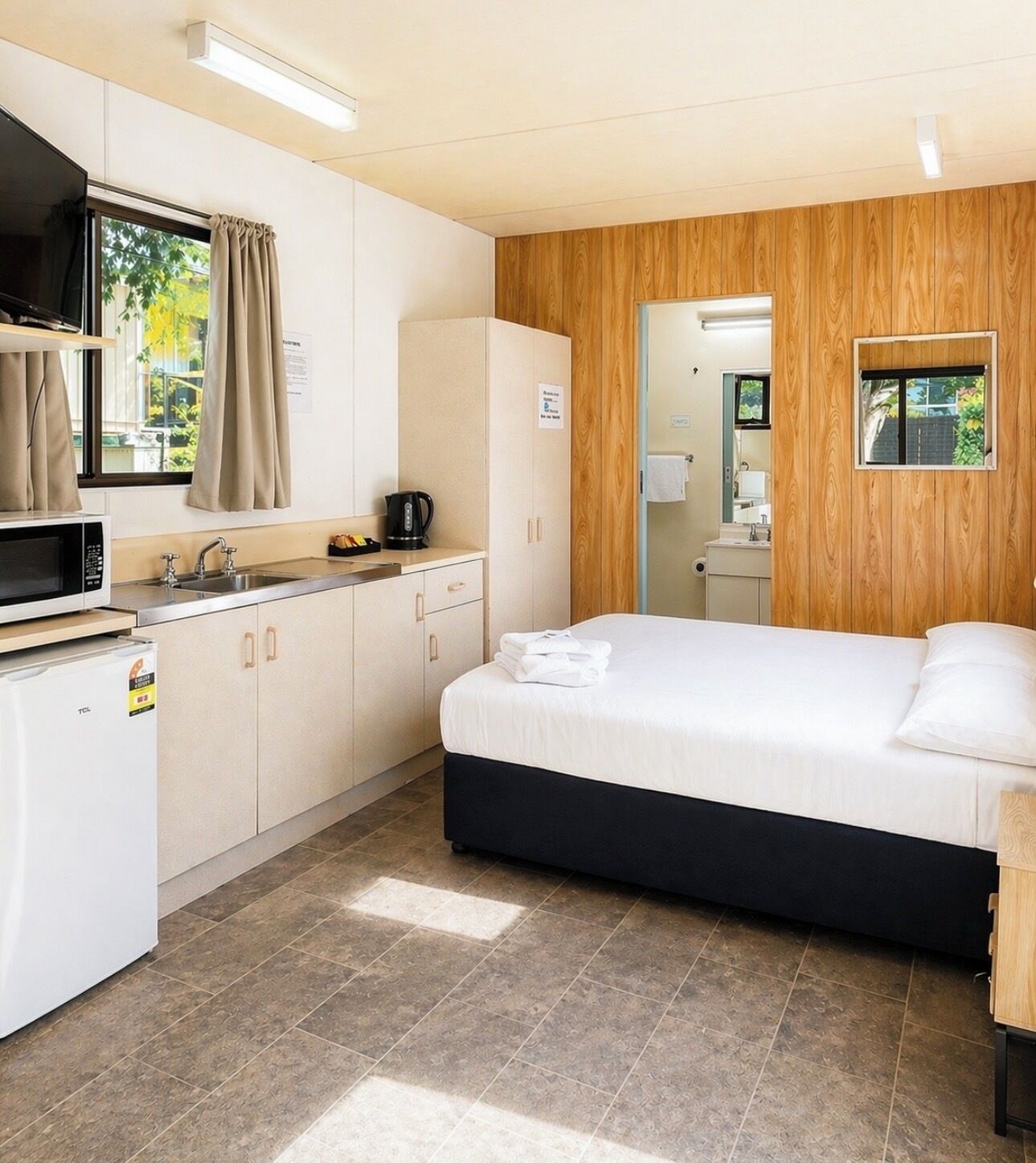 Habitación de hotel con cama, kitchenette, espejo y ventana con cortinas.