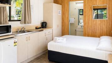 Habitación de hotel con cama, kitchenette, espejo y ventana con cortinas.