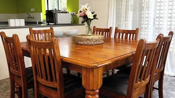 A dining area with a wooden table and chairs, a vase with flowers, and a kitchen in the background.