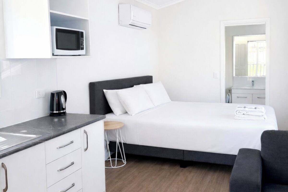 Habitación de hotel moderna con kitchenette, cama, ventilador de techo y vista al exterior.