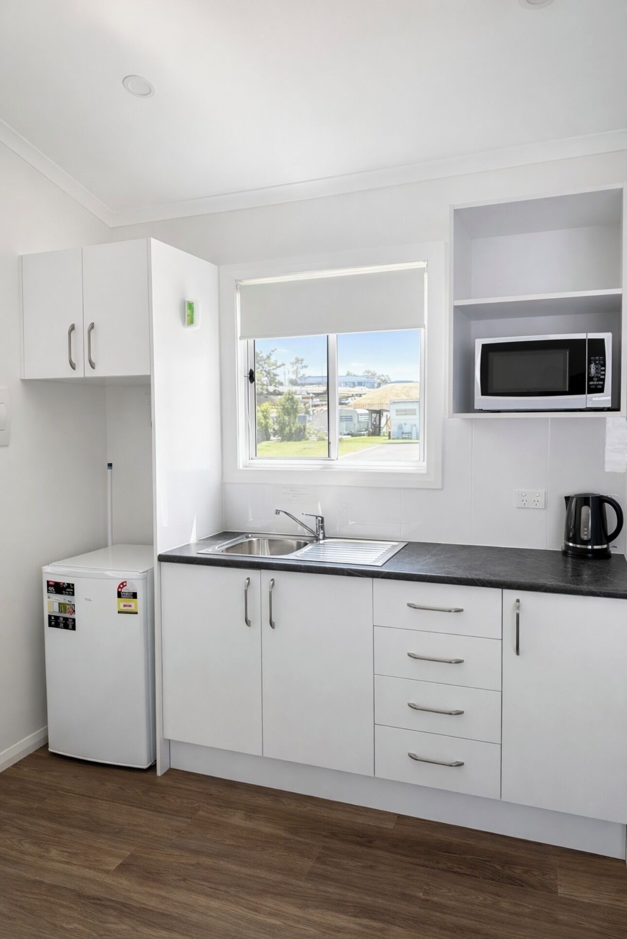 Una cocina moderna con armarios blancos, microondas integrado, un lavamanos y una ventana con vistas.