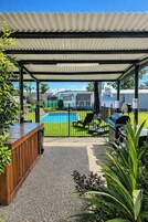 A covered outdoor area with a pool, chairs, and a barbecue grill.