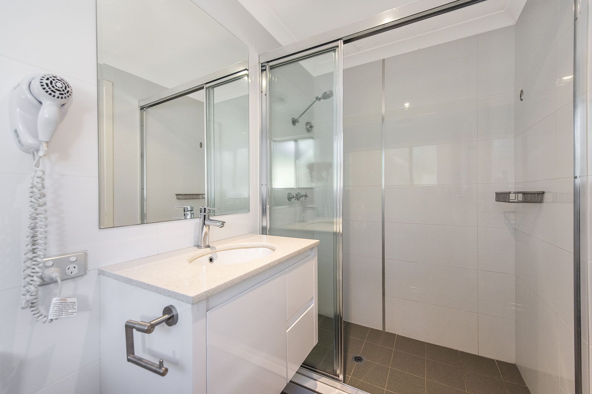 A modern bathroom with a glass shower enclosure, a white sink, and a hairdryer mounted on the wall.