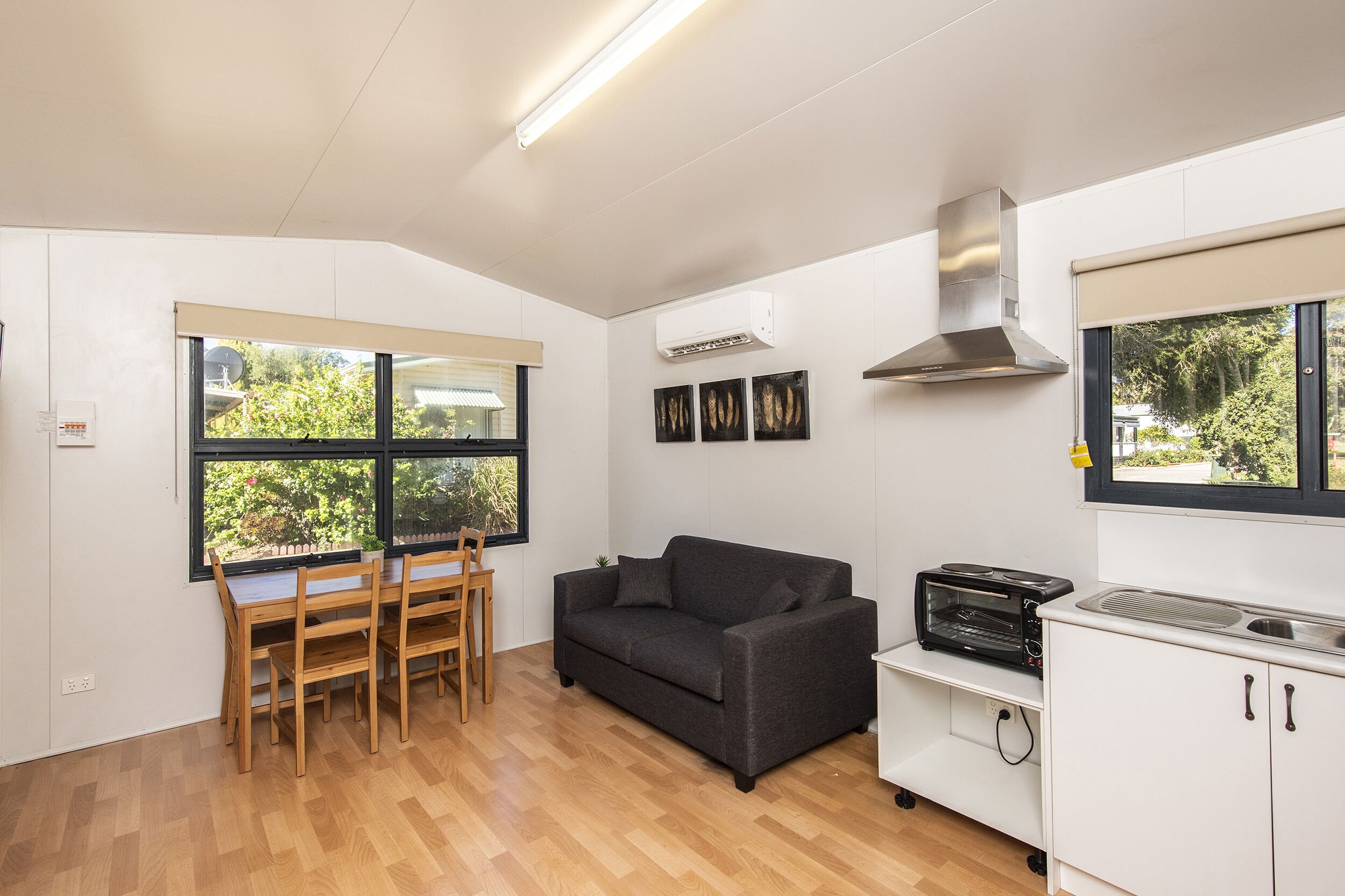 A compact kitchen with a dining area, a sofa, and a window with a view of greenery.