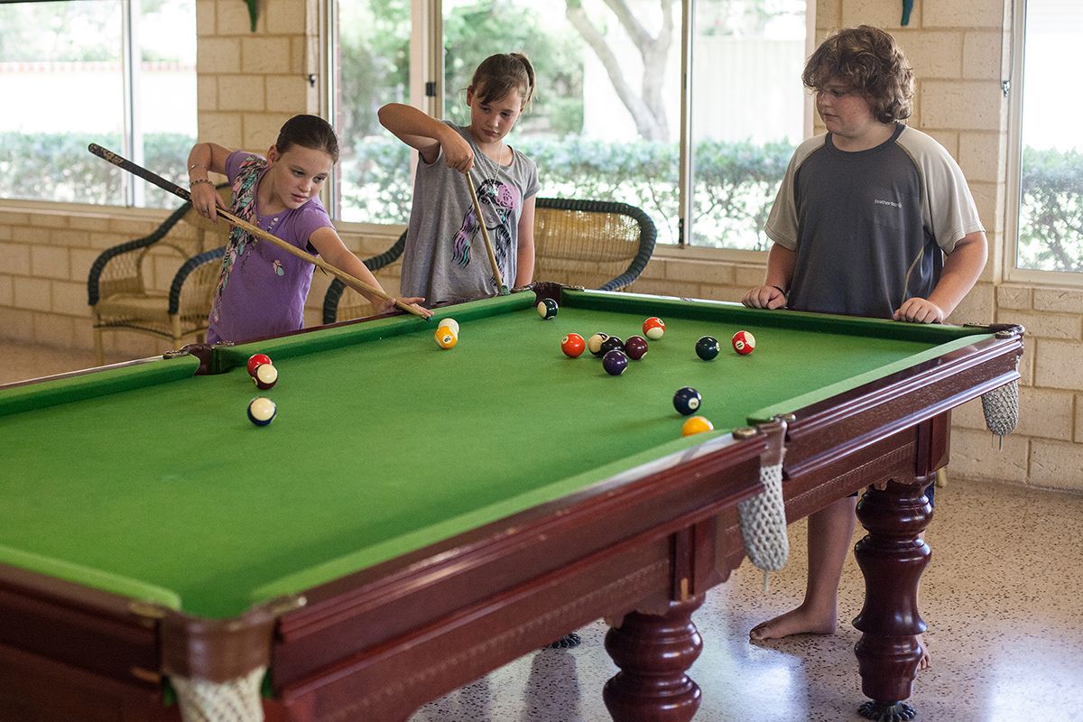 A pool table with balls, a wooden table, and a window in the background.
