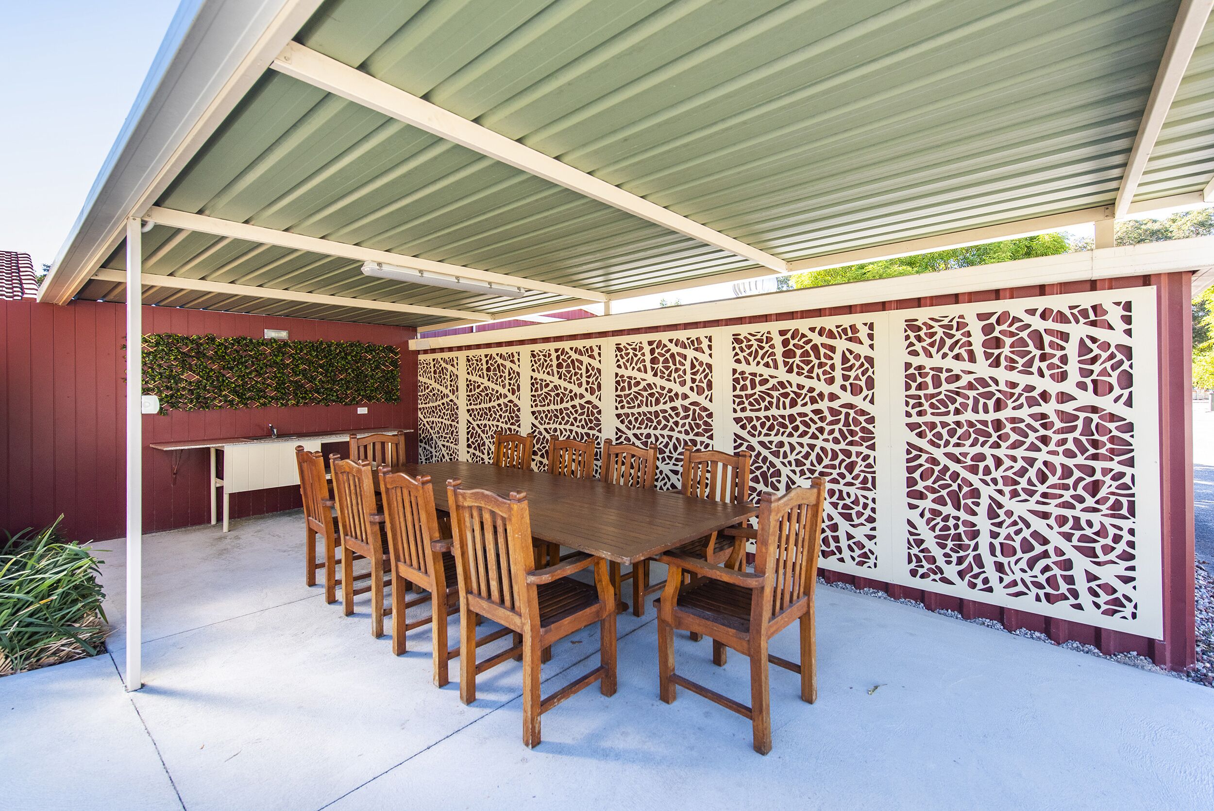 Une terrasse extérieure avec une table et des chaises en bois, un barbecue et un mur décoratif.
