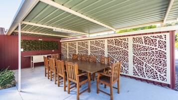 Un patio al aire libre con una mesa y sillas de madera, una parrilla y un muro decorativo.